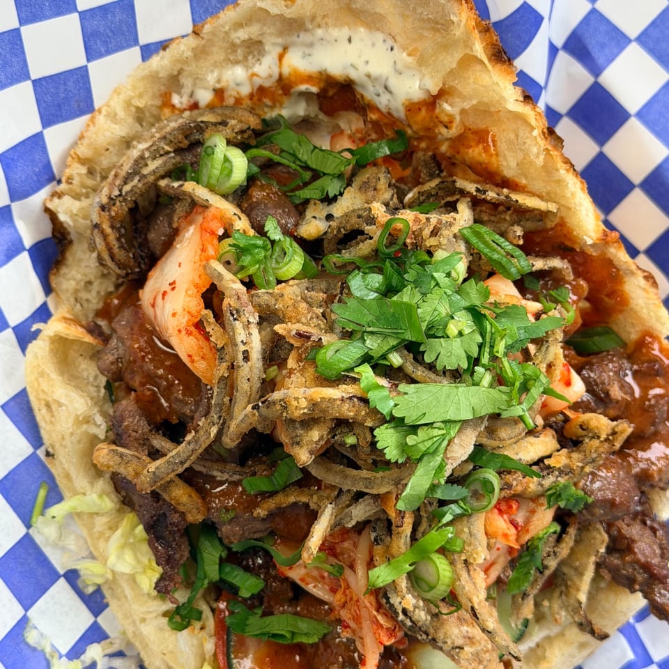 A close-up of a Little Bear Street Eats pizza with beef, kimchi, fried onions, and cilantro.