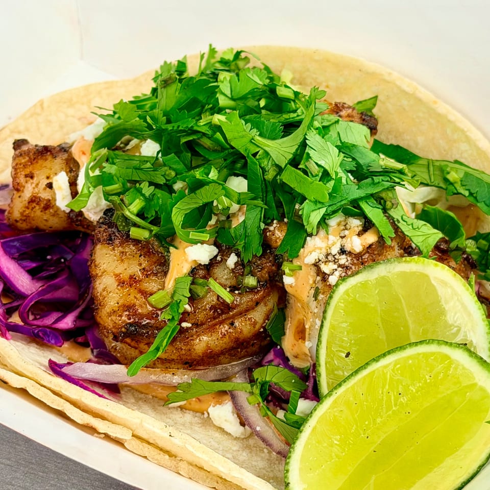 Close-up of a taco with grilled meat, purple cabbage, cilantro, sauce, and lime wedges.
