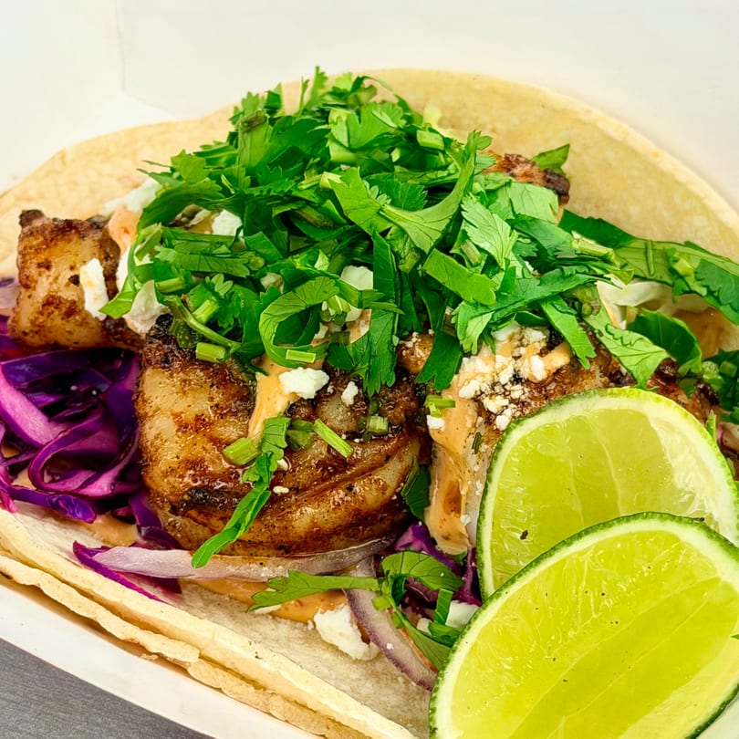 Close-up of a taco with grilled meat, purple cabbage, cilantro, sauce, and lime wedges.
