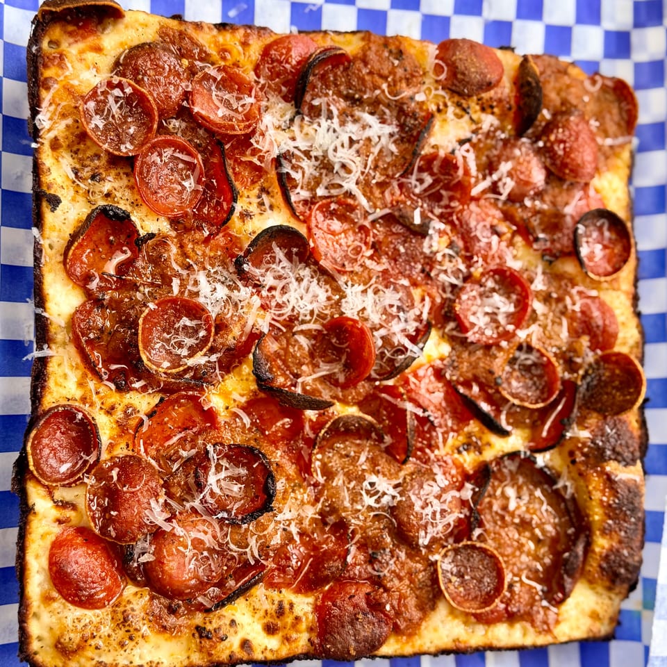 Square pepperoni pizza from Little Bear Street Eats, topped with grated cheese on blue and white checkered paper.