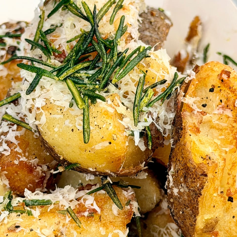 Crispy roasted potatoes topped with fresh rosemary and grated Parmesan cheese.