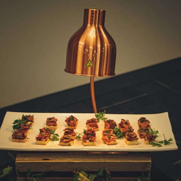 Little Bear Street Eats' bruschetta appetizers under a copper heat lamp, garnished with parsley.