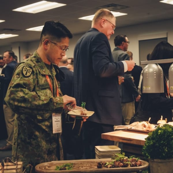 A man in military fatigues serves himself food from a buffet line at an event.