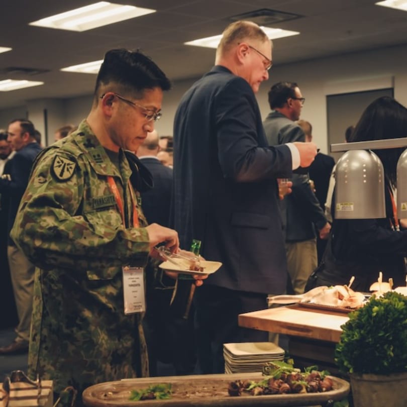 A man in military fatigues serves himself food from a buffet line at an event.