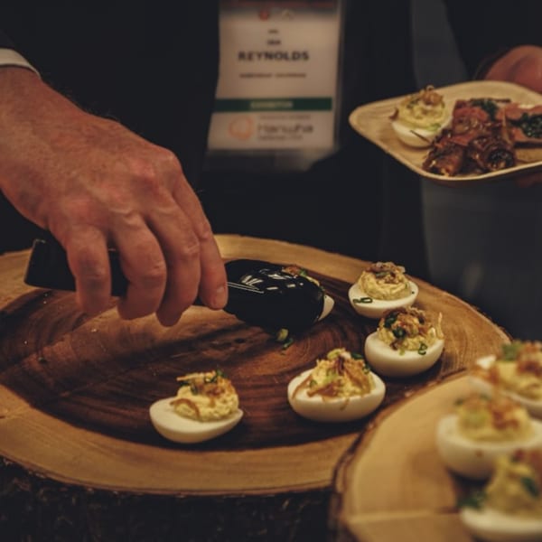 A person serving deviled eggs and other appetizers from a wooden platter.