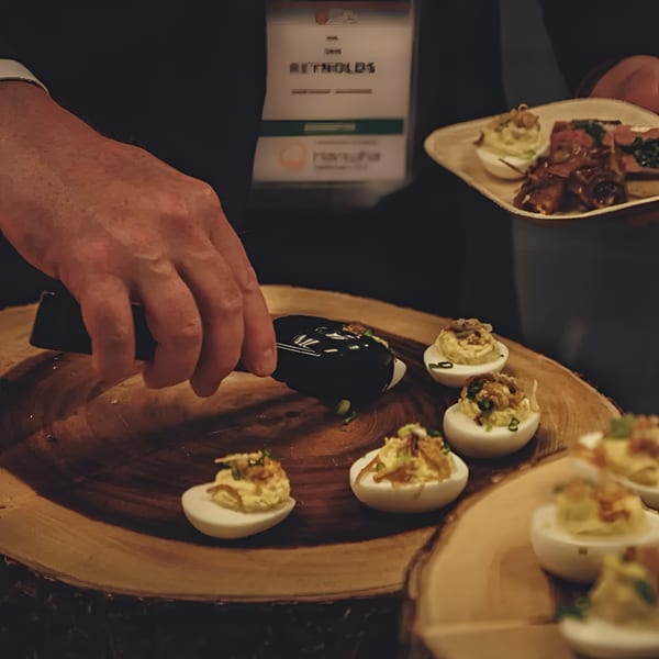 A person using tongs to serve deviled eggs from a wooden platter at an event.